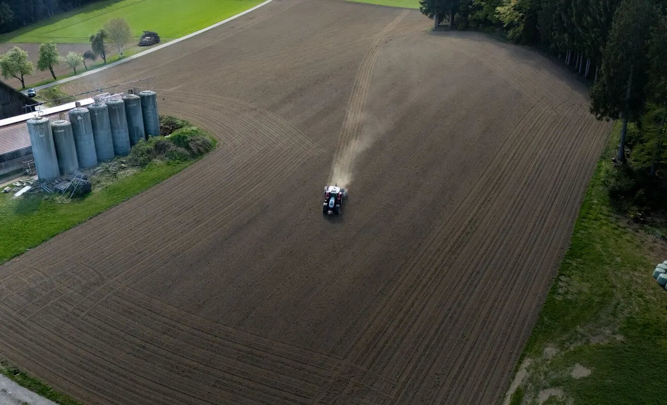 Traktor zieht Spuren über den Acker neben den Silos