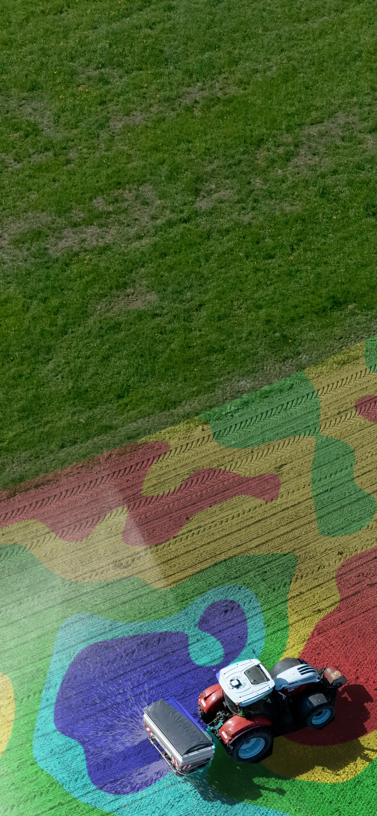 Traktor mit Zweischeiben-Düngerstreuer auf einem Acker, über dem Feld eine Applikationskarte mit fünf farbigen Nährstoffzonen