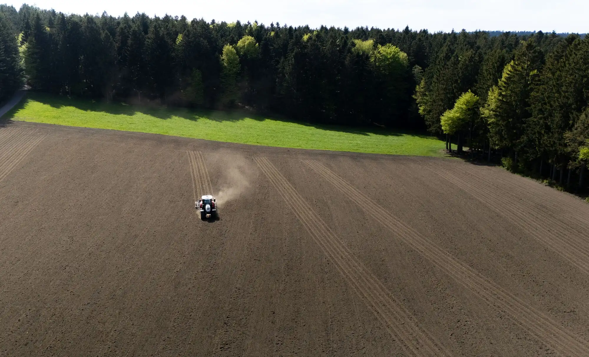 Traktor bei der Feldarbeit mit Spurführung – Luftaufnahme am Waldrand